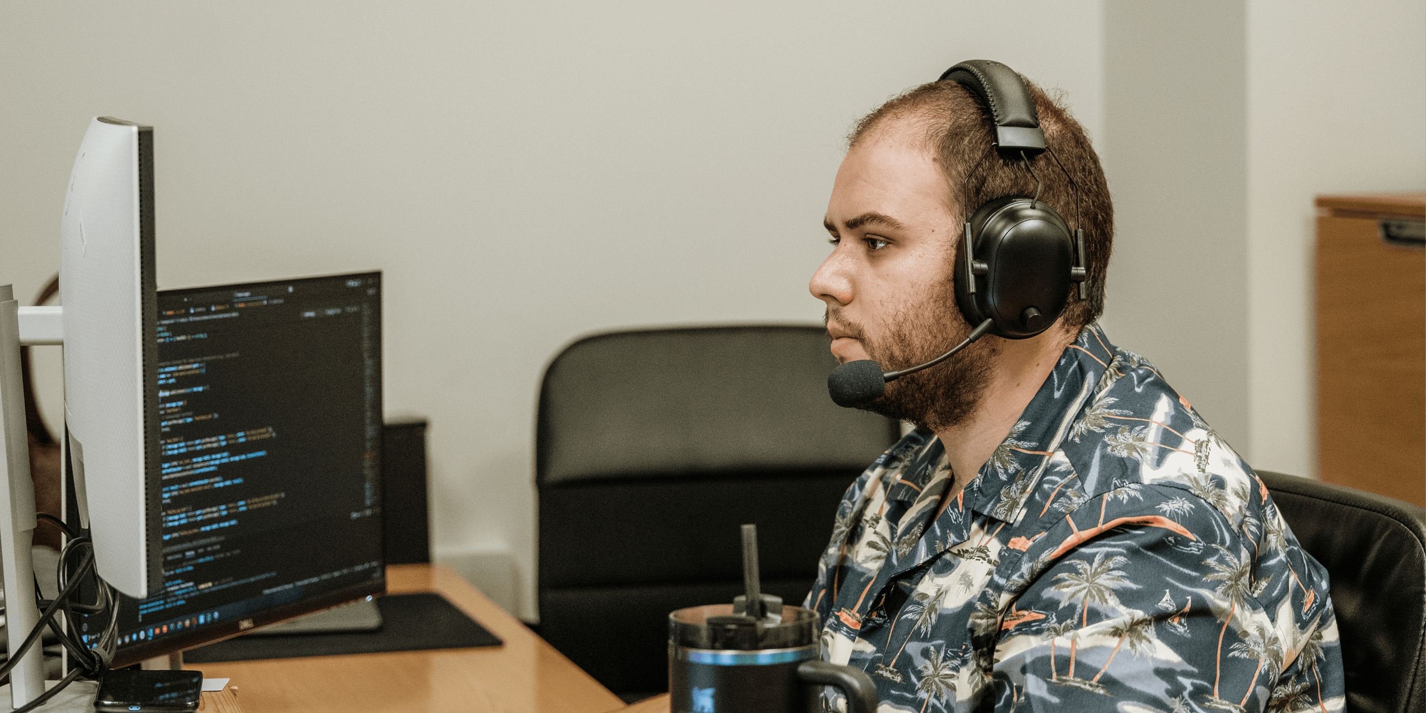 Daniel with headphones working on in computer with two monitors, on Mediaweb's office